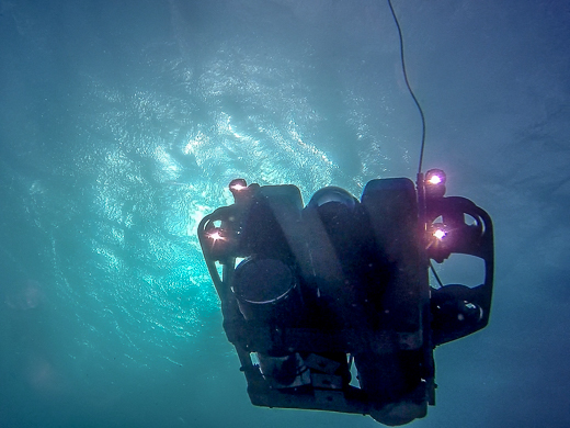 A view from underneath a mini remotely operated vehicle looking towards sunlight shining through the water surface.  